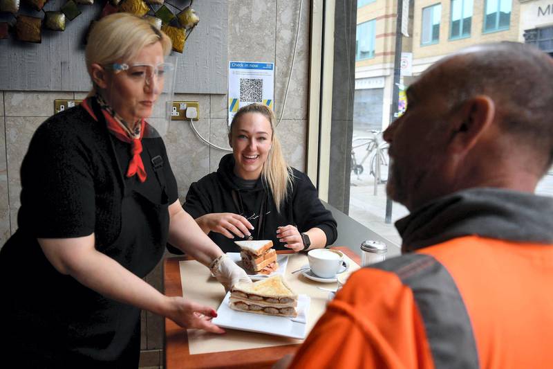 A worker places a customer's breakfast order of a sausage sandwich at a table inside Barbarella's cafe in London as Covid-19 lockdown restrictions ease across the country on May 17, 2021. / AFP / DANIEL LEAL-OLIVAS
