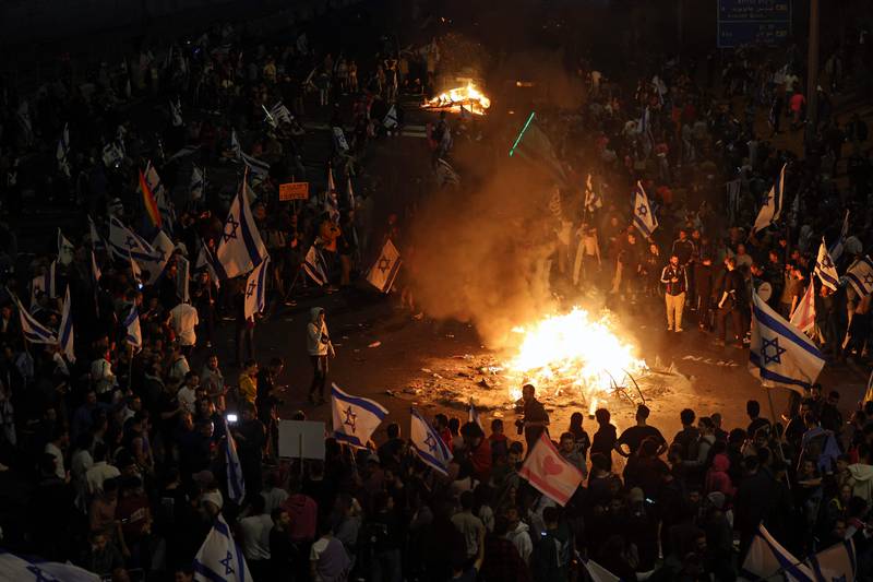 The protesters in Tel Aviv hold Israeli flags as they gather around a bonfire. AFP