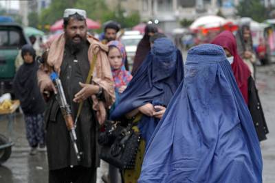 Women walk through the old market as a Taliban fighter stands guard, in the city of Kabul, Afghanistan. AP