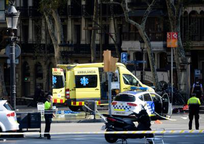 A policemen and a medical staff member stand near police cars and an ambulance in a cordoned-off area, after a van ploughed into a crowd in Barcelona. Josep LAGO / AFP.