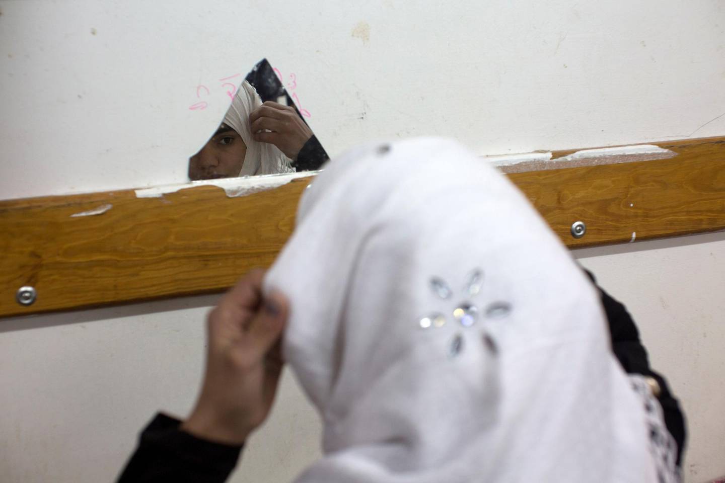 A young Palestinian girl prepares herself for school as she pins her headscarf in place using a tiny broken mirror that is on the wall at the UN school in Beit Hanoun in northern Gaza, December 30,2014. Thousands of Palestinians in Gaza remained displaced by the war (Photo by Heidi Levine/Sipa Press).