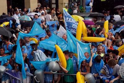 Manchester City fans take shelter from the rain ahead of the parade. PA 