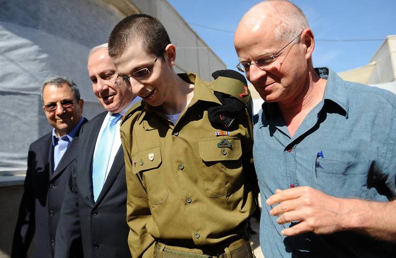 EDITOR'S NOTE - RESTRICTED TO EDITORIAL USE - MANDATORY CREDIT "AFP PHOTO/PMO " - NO MARKETING NO ADVERTISING CAMPAIGNS - DISTRIBUTED AS A SERVICE TO CLIENTS 
A handout picture released by the Israeli Prime Minister Office shows Israeli soldier Gilad Shalit (C) being hugged by his father Noam (R) for the first time in five years as they walk alongside Israeli Prime Minister Benjamin Netanyahu and Defense Minister Ehud Barak at the Tel Nof airbase near Tel Aviv on October 18, 2011 following his release following 5 years of Hamas captivity under a landmark Egyptian-mediated deal that will see Israel release a total of 1,027 Palestinian prisoners. AFP PHOTO/PMO/HO (Photo by PMO / PMO / AFP)