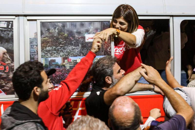 A Lebanese anti-government protester shakes hands with another supporter from a "revolution" bus on a cross-country trip from the north to the south of the country, as it was met with counter-protesters in the southern city of Sidon on November 16, 2019. The "revolution" bus took off in Tripoli in the north of Lebanon on a coastal ride towards the south, and is partially aimed at countering the stigma surrounding an attack on a similar bus in 1975 in Beirut's Ain al-Rummaneh area that is said to have triggered the Lebanese civil war which fragmented the country. / AFP / Mahmoud ZAYYAT
