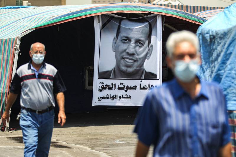 Men walk past a mourning tent bearing the poster of slain Iraqi extremism expert Husham Al Hashimi, who was shot outside his house this week. AFP
