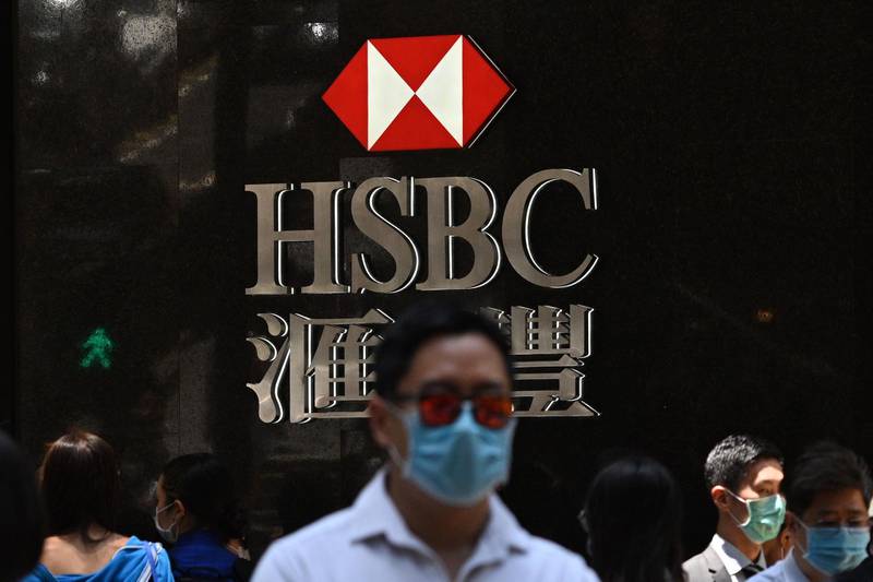Pedestrians wear face masks as they walk past HSBC signage outside a branch of the bank in Hong Kong on April 28, 2020. HSBC on April 28 said first quarter pre-tax profits almost halved as the banking giant was battered by the global coronavirus pandemic while it embarked on a major restructuring. / AFP / Anthony WALLACE
