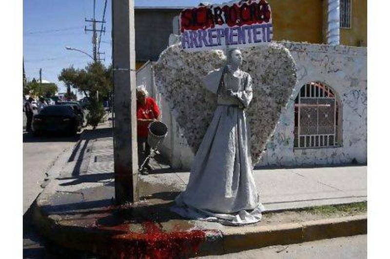 A young member of the Christian church Psalm 100 dressed as an angel holds a sign reading "Hitmen, believe and repent" while a woman throws a bucket of water on a puddle of blood at a crime scene on Saturday where a man was shot dead in Ciudad Juarez. Jose Luis Gonzalez / Reuters
