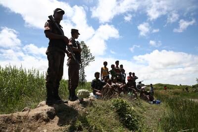Bangladeshi border guard personnel keep watch over Rohingya, sitting, as they stop them from crossing over to the Bangladesh side of the border at Ghumdhum, Cox's Bazar, Bangladesh, Sunday, Aug.27, 2017. Several hundred Rohingya trying to flee Myanmar got stuck in a "no man's land" at one border point barred from moving farther by Bangladeshi border guards. (AP Photo/Mushfiqul Alam)