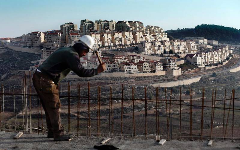A man works on a construction site in Bethlehem, Palestine, as illegal settlements tower in the distance (AFP / AHMAD GHARABLI)