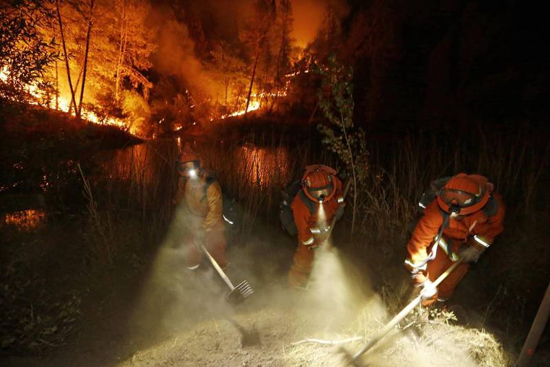 Firefighters in northern California create a firebreak near a home in Middletown. Two of the western state’s fastest-burning wildfires in decades overtook several towns, killing at least one person and destroying hundreds of homes, vehicles and businesses. Elaine Thompson / AP Photo