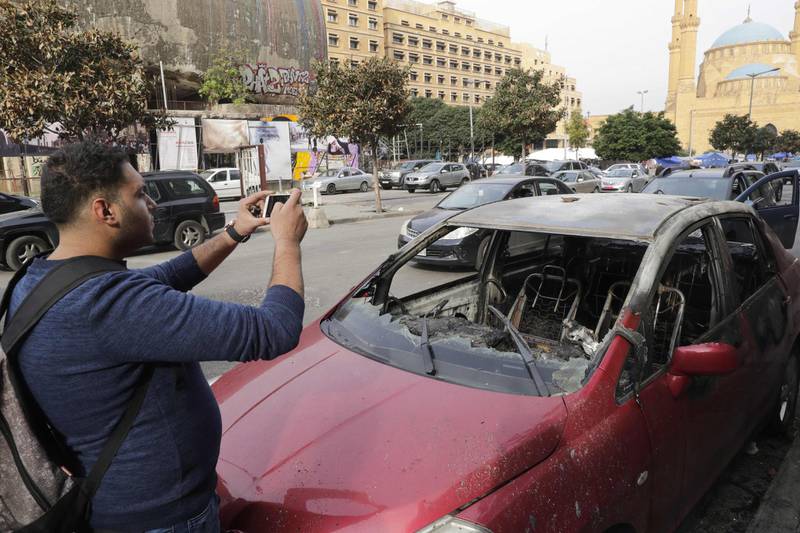 A Lebanese man takes pictures of a damaged car after a night of clashes between supporters of the Shiite groups Hezbollah and Amal and anti-government demonstrators in the capital Beirut. AFP