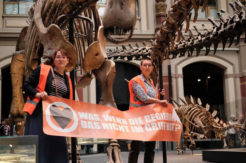 Two environmental activists of Last Generation glue themselves to metal bars around a display of dinosaur skeletons and holding a banner reading "what if the government does not have it under control" in the Berlin's Natural History Museum, in Berlin on October 30. AFP
