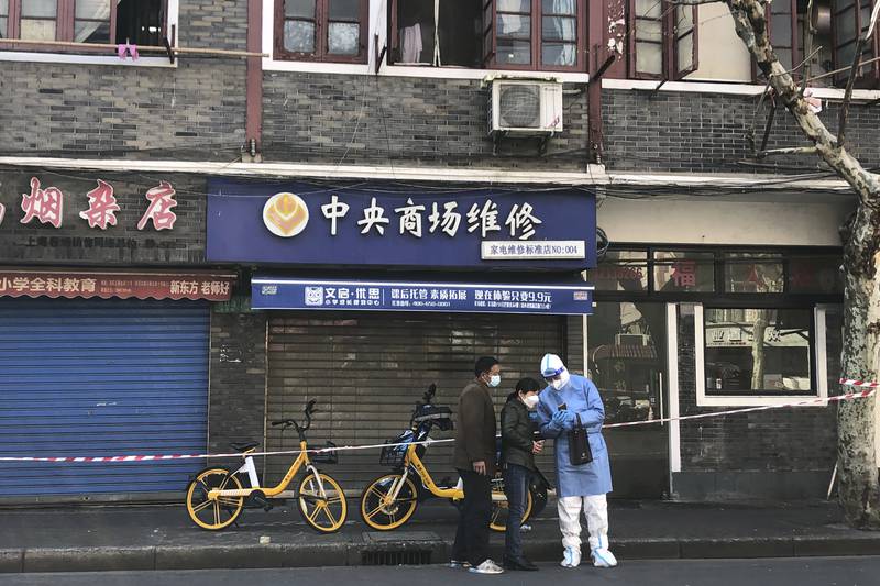 A worker in protective gear chats with residents outside shuttered shops in the Jingan district of western Shanghai.   AP
