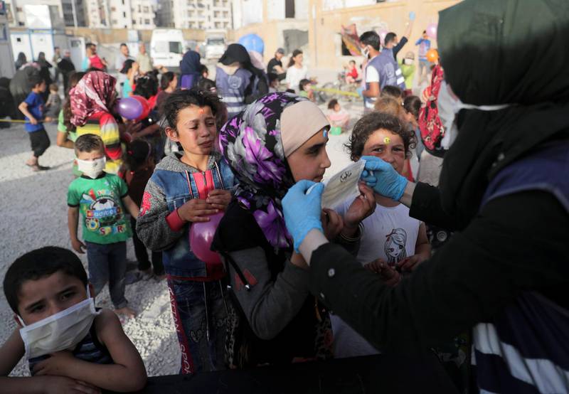 A volunteer from the International Association for Relief and Development (ONSUR) distributes face masks to internally displaced children, ahead of the Eid al-Fitr holiday, at an IDP camp in Idlib, Syria. Reuters