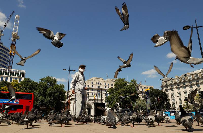 A man wearing a face mask feeds pigeons in front of Marble Arch, as the outbreak of the coronavirus disease (COVID-19) continues in London, Britain June 22, 2020. REUTERS/John Sibley