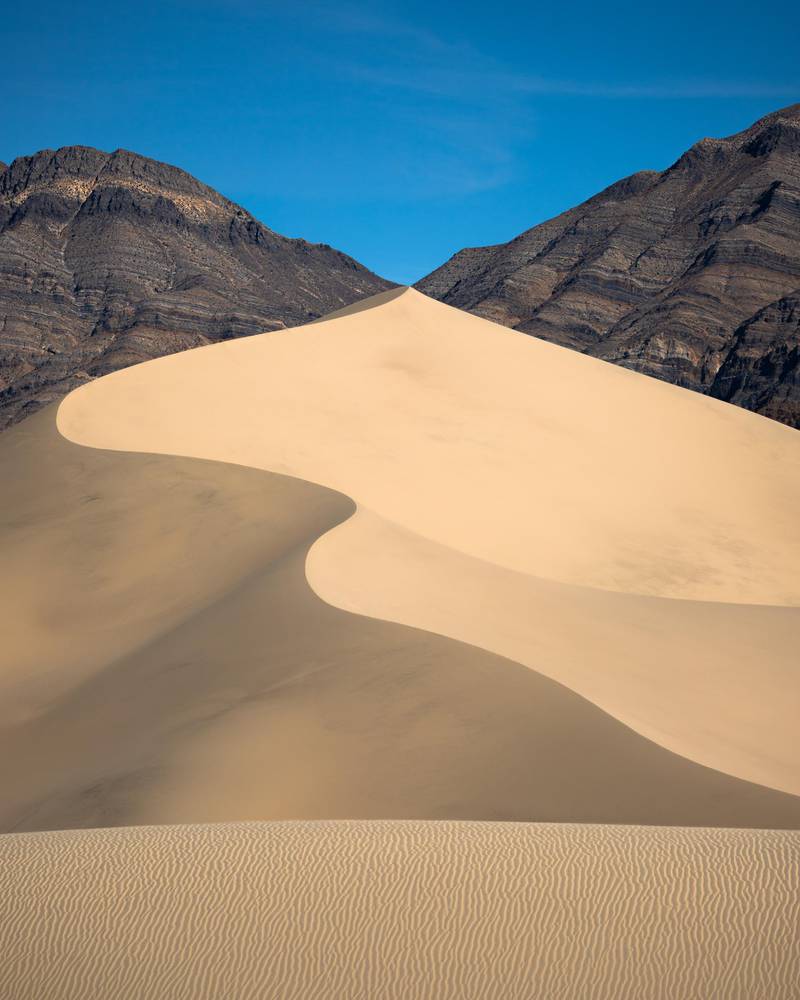 A snaking dune in Death Valley meets the saddle of the surrounding mountains.

