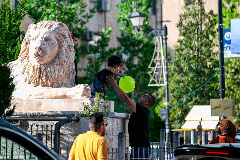A woman uses a phone to film a man playing with a girl by a statue of a lion in the centre of the West Bank city of Ramallah, after the Palestinian Authority announced an end to its two-month coronavirus lockdown. AFP