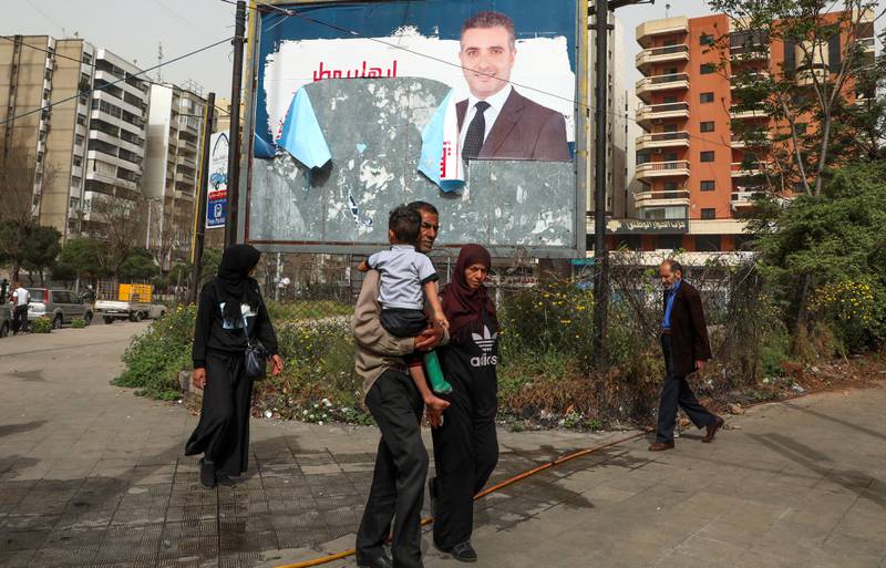 People walk past a torn campaign banner, ahead of parliamentary election that are scheduled for May 15, in Tripoli. Reuters