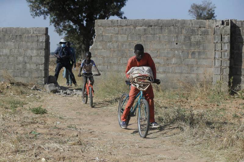 Children ride on bicycles past a wall broken by the extremists to kidnap the pupils. AP Photo