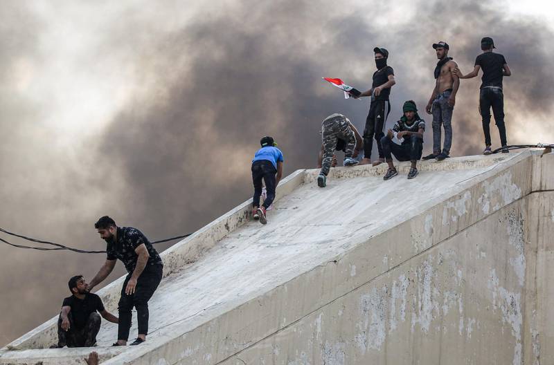 Protesters stand on a concrete arch connected to a burning building between the capital Baghdad's Tahrir Square and the high-security Green Zone district. AFP