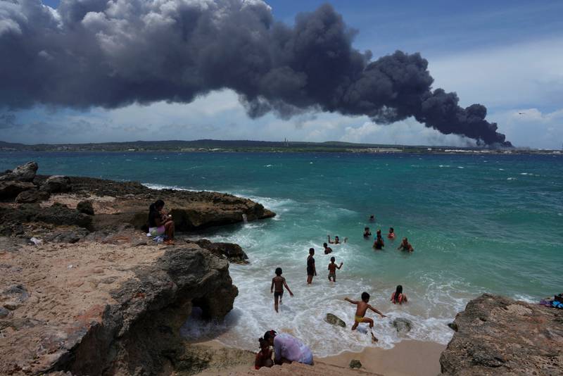 People enjoy the beach while smoke rises from the fire at fuel storage tanks that exploded near Cuba's supertanker port in Matanzas. Reuters