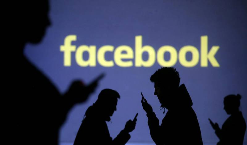 Silhouettes of mobile users are seen next to a screen projection of Facebook logo in this picture illustration taken March 28, 2018.  REUTERS/Dado Ruvic