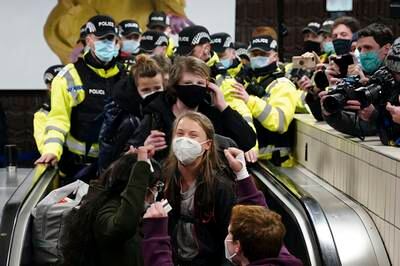 A masked Greta Thunberg is escorted down the escalator. AP Photo