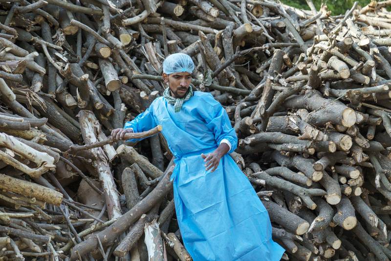 A worker wearing personal protective equipment sorts funeral pyre wood at a crematorium in New Delhi, India. Bloomberg