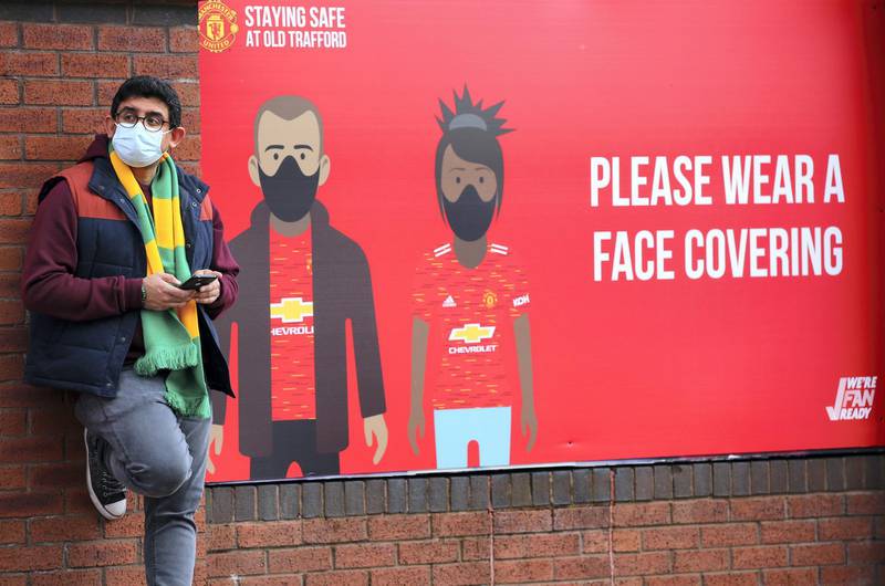 MANCHESTER, ENGLAND - MAY 18: A Manchester United fan is seen wearing a face mask outside the stadium next to a sign saying "Please wear a face covering" prior to the Premier League match between Manchester United and Fulham at Old Trafford on May 18, 2021 in Manchester, England. A limited number of fans will be allowed into Premier League stadium's as Coronavirus restrictions begin to ease in the UK following the COVID-19 pandemic. (Photo by Alex Livesey/Getty Images)