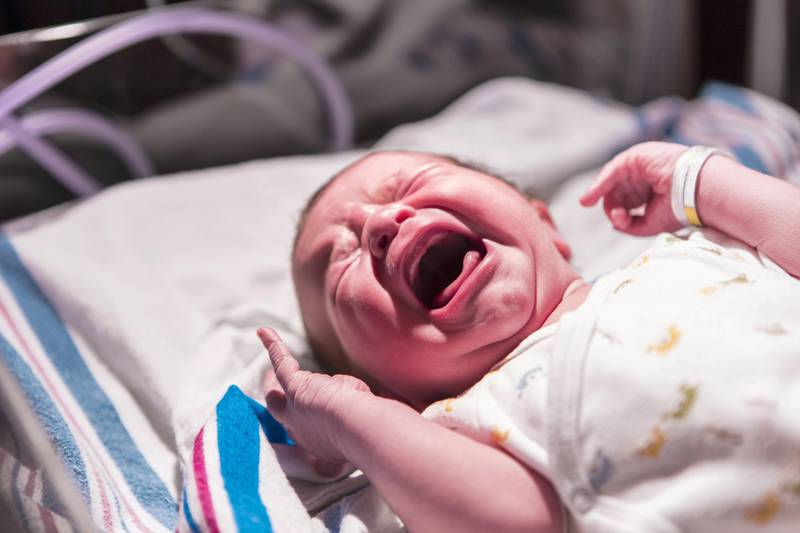 Caucasian newborn baby crying in hospital crib