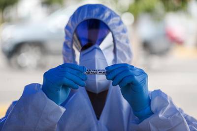 A healthcare worker holds a sample of a nasal swab after testing a passenger at a drive-thru new coronavirus testing site outside a supermarket in Santiago, Chile. AP Photo