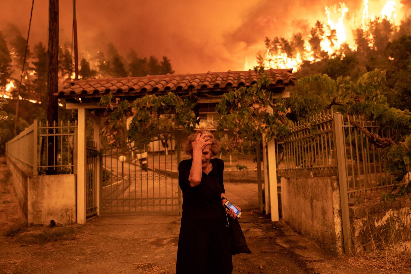 A woman flees her house in the Greek village of Gouves as a wildfire approaches. 