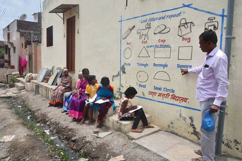 Children in an Indian village gather around their teacher as he delivers a lesson painted on a wall. It is part of efforts to help poor pupils keep up with their education amid the coronavirus pandemic.