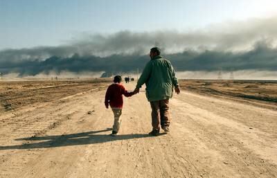 March 29, 2003: A man and child walk on a road near the entrance of the besieged city of Basra as oil fires burn in the distance. Baath Party loyalists take up positions in Basra, Iraq's second largest city, making it a target of the US-led war on Iraq. Getty 