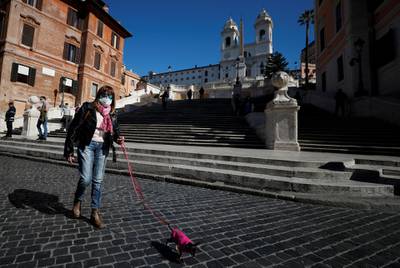 A woman wears a face mask as she walks a dog in Rome, Italy. Reuters