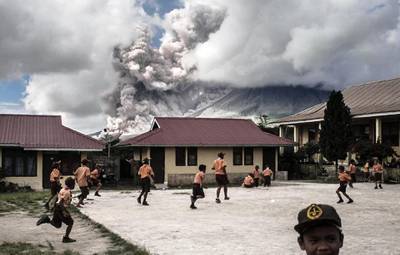 Indonesian school children play outside as mount Sinabung volcano spews thick volcanic ash as seen from Karo, North Sumatra province. AFP Photo / February 10, 2017.