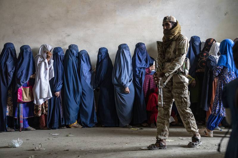 A Taliban fighter stands guard as women wait to receive food rations distributed by a humanitarian aid group in Kabul, Afghanistan. AP
