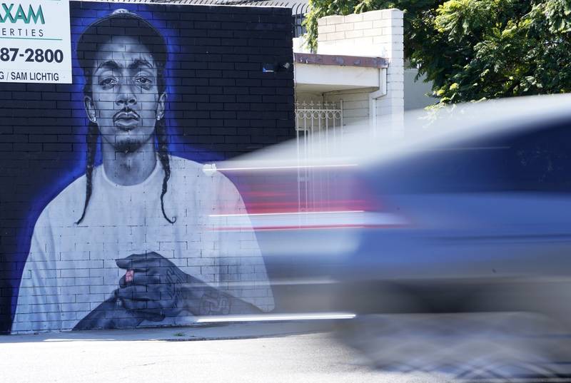 A car blurs past a street mural of Hussle. AP