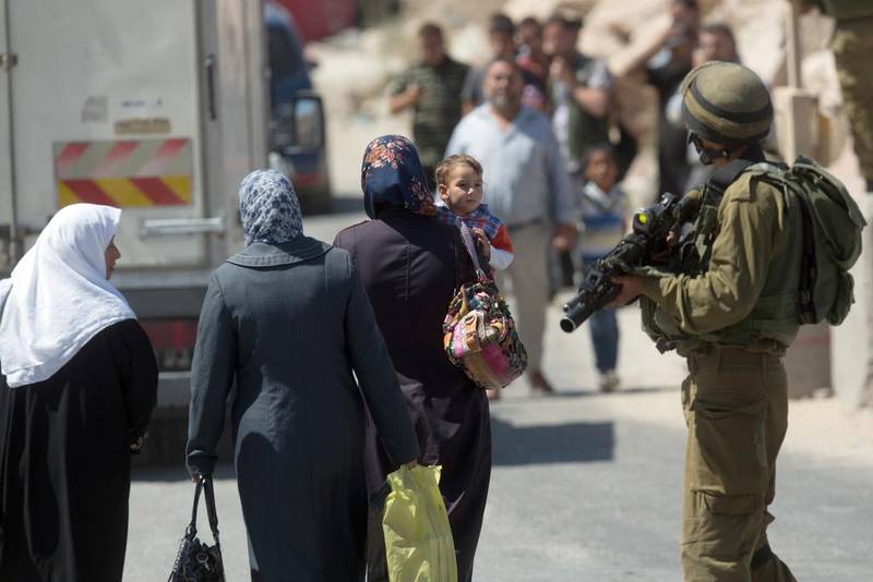 Palestinians walk past an Israeli soldier at a checkpoint in he West Bank town of Hebron, where Israeli security forces stand guard on June 15, 2014, as Israel broadened the search for three teenagers believed kidnapped by militants and imposed a tight closure of the town. AFP PHOTO/MENAHEM KAHANA