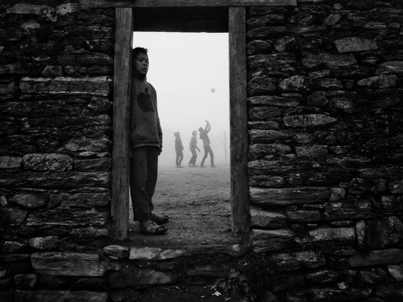 Volleyball is the national sport of Nepal, and is particularly popular in the higher mountains. This entrance through the stone wall leads to a public-school compound where villagers play volleyball once classes have finished. When I made this image, the ground was engulfed with fog, silhouetting the volleyball-playing men.
