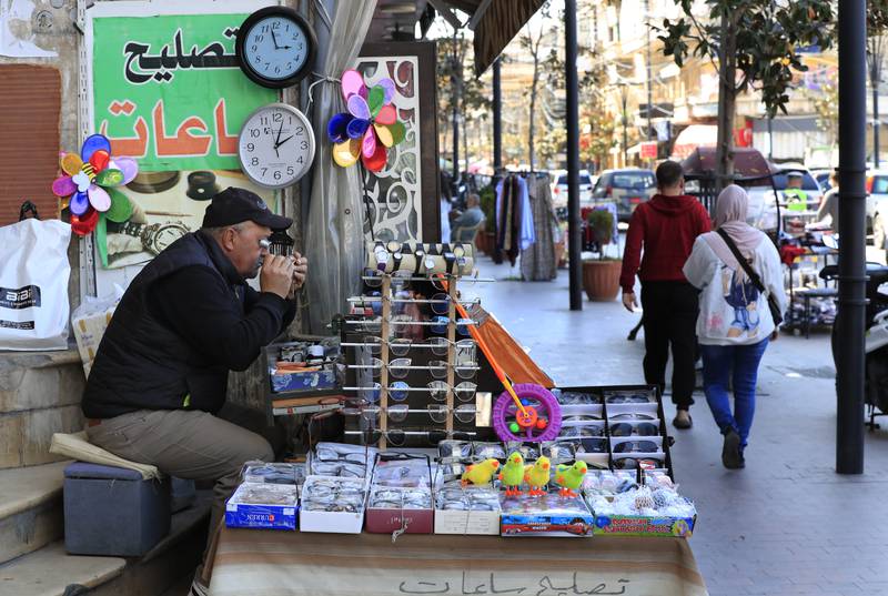 Salah Nasab, a Lebanese street vendor who also sells and repairs clocks, sits next to two clocks that show different times in the southern port city of Sidon on Monday. AP