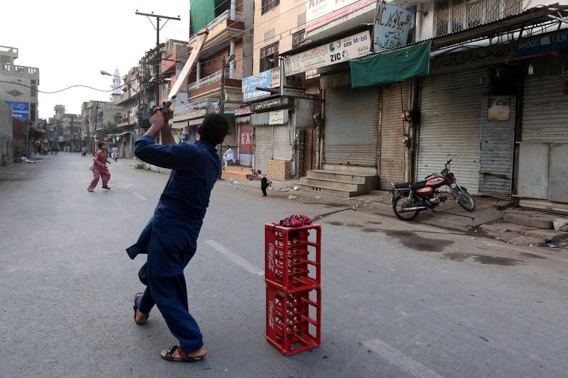 Pakistani boys play cricket on a road near a restricted area that is sealed in smart lockdown, in Lahore, Pakistan. EPA