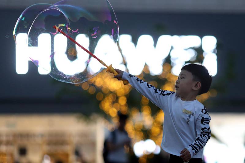 In this photo taken Monday, May 20, 2019, a child plays with bubbles near the logo for tech giant Huawei in Beijing. The Trump administration's sanctions against Huawei have begun to bite even though their dimensions remain unclear. U.S. companies that supply the Chinese tech powerhouse with computer chips saw their stock prices slump Monday, and Huawei faces decimated smartphone sales with the anticipated loss of Google's popular software and services. (AP Photo/Ng Han Guan)
