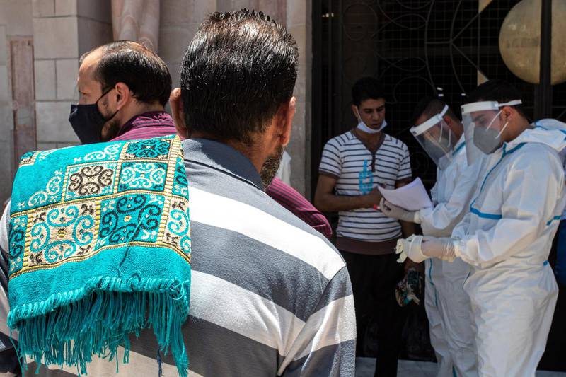 A  man stands with a prayer rug on his shoulder as Jordanian medics get ready to perform a coronavirus test, in front of Husseini Mosque, before the Friday prayer in central Amman, Jordan.  EPA