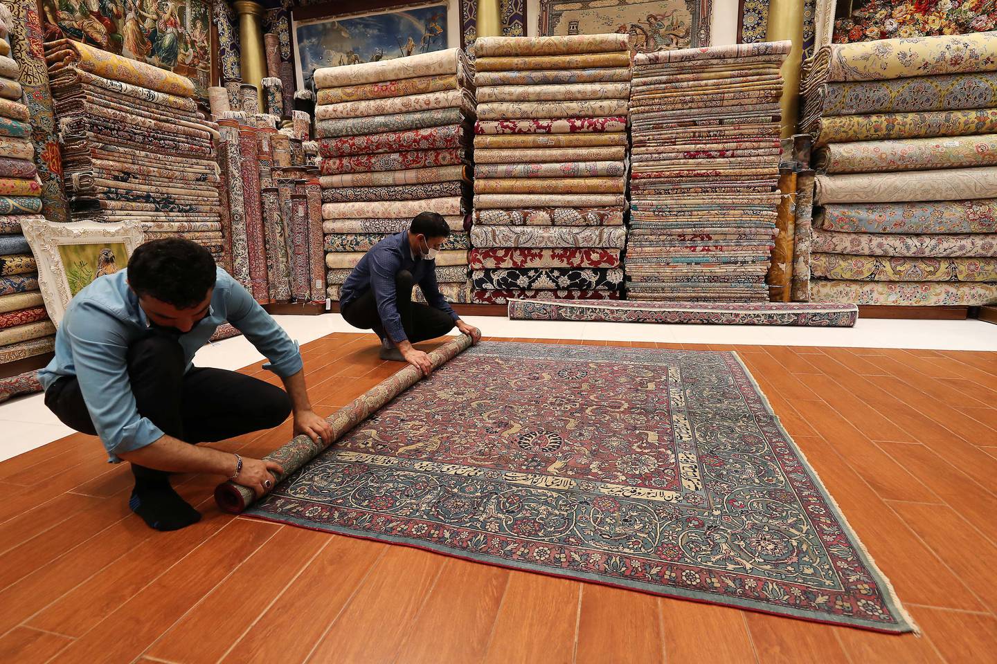 Shopkeepers roll a carpet at the Dubai Mall. Carpets from around the world, including Iran, are sold in the UAE Pawan Singh / The National