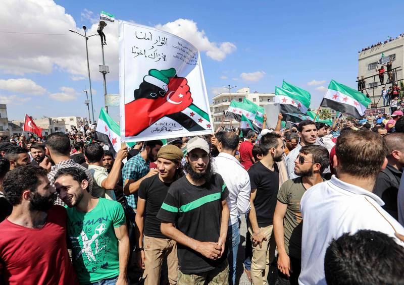 Syrian men raise a banner depicting two hands embracing each other painted in the flag of the opposition and the Turkish flag and with a caption reading in Arabic "the revolutionaries are our hope and the Turks are our brothers", during an anti-government demonstration attended by residents of the rebel-held northern city of Idlib and its surrounding towns in a main square in Idlib on September 14, 2018.  / AFP / OMAR HAJ KADOUR
