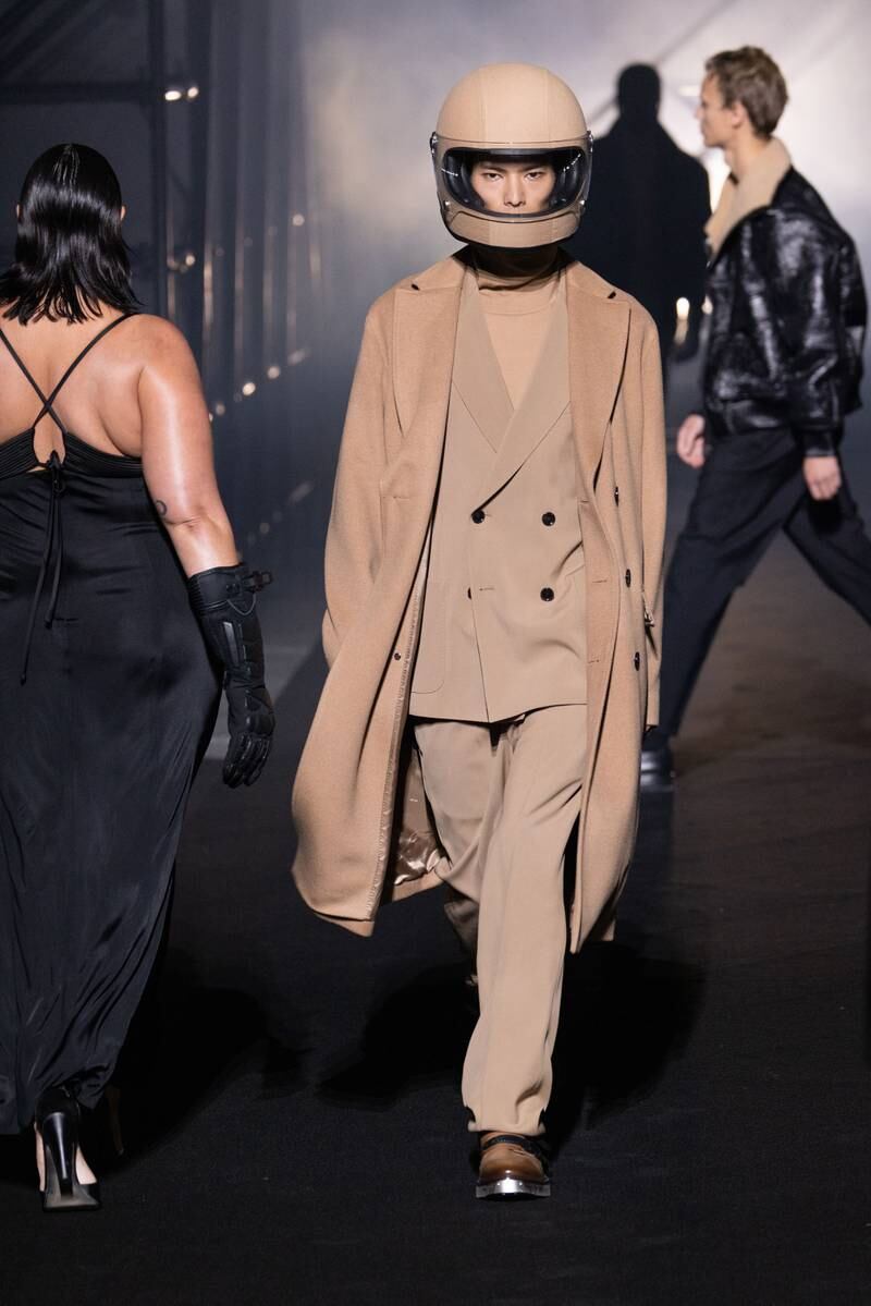 A model sports a helmet and coat over a double-breasted suit, in various shades of tan.