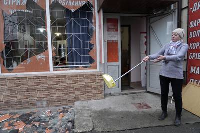 A Kiev resident sweeps up debris after Russian shelling. AP