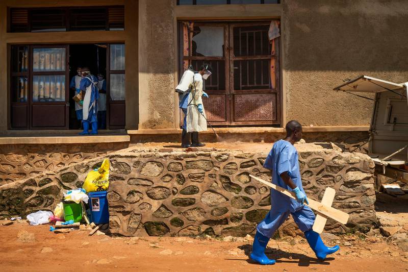 A morgue employee walks with a cross past others disinfecting the entrance to the morgue in Beni, Congo. AP
