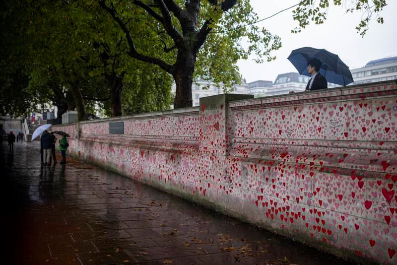 A man sheltering beneath an umbrella looks out from above the National Covid Memorial Wall in London. Getty Images